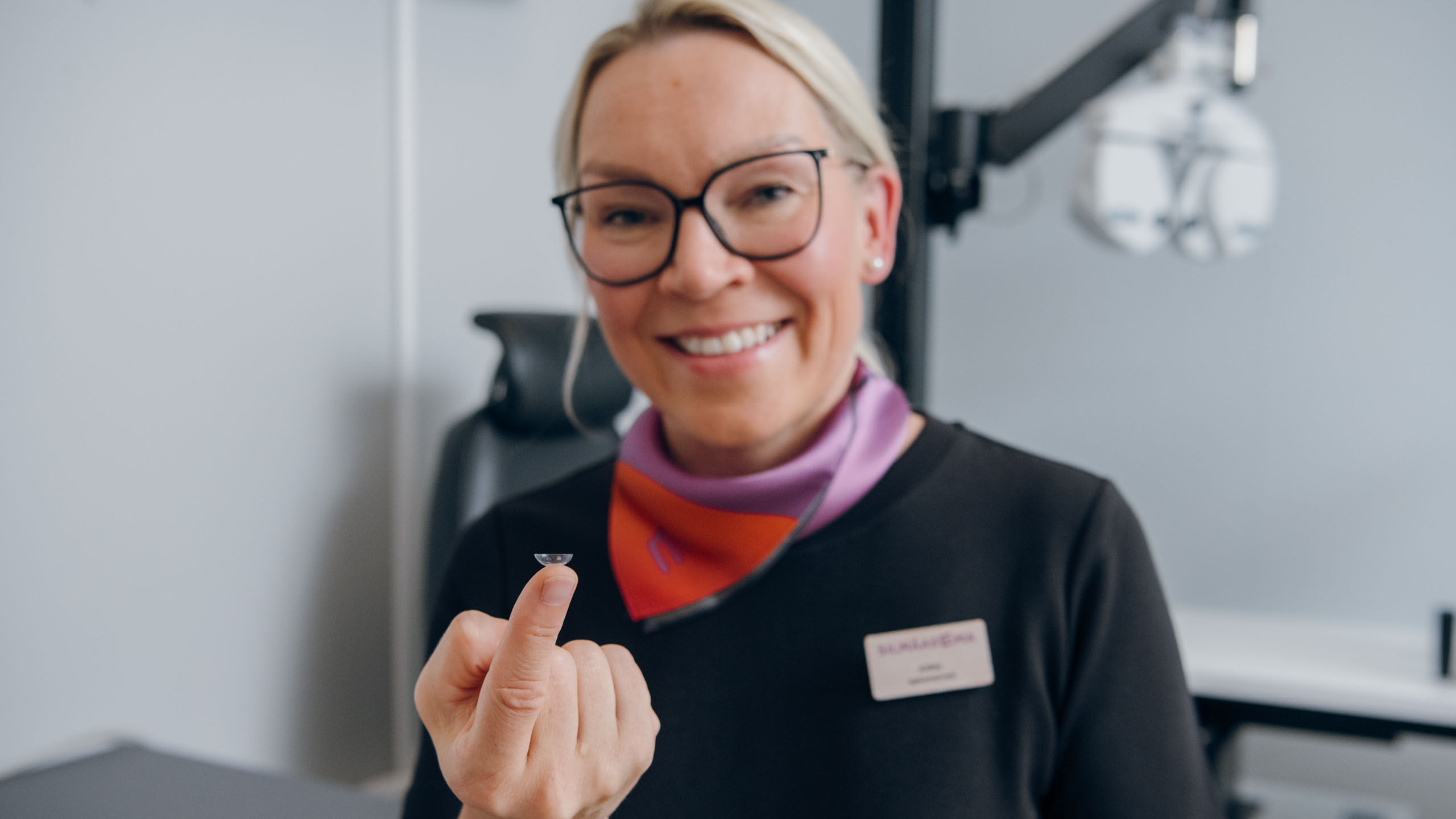Optikko pitelee sormen p&auml;&auml;ss&auml; piilolinssi&auml;.